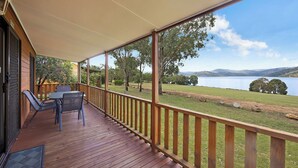 A wooden deck with a table and chairs, overlooking a grassy area and a body of water. - Reflections Grabine Lakeside - Holiday Park (Bigga)