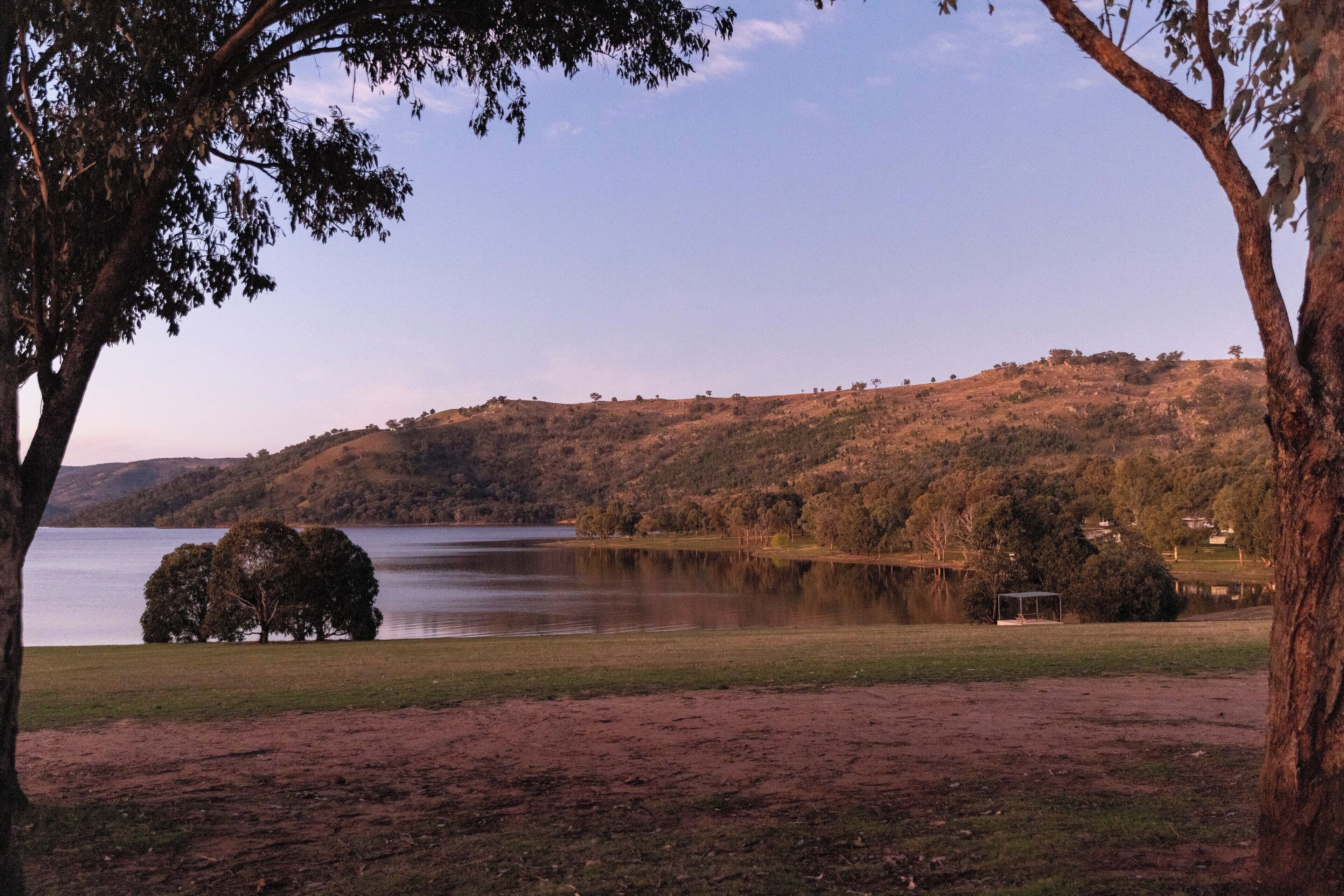 A lake surrounded by hills with a few trees and a small structure in the distance.