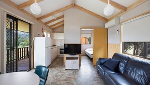 A compact living space with a dining area, a sofa, a television on a wooden stand, and a kitchen in the background. - Reflections Grabine Lakeside - Holiday Park (Bigga)