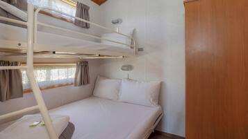 A bunk bed with white bedding and curtains, a wooden wardrobe, and a window with curtains.
