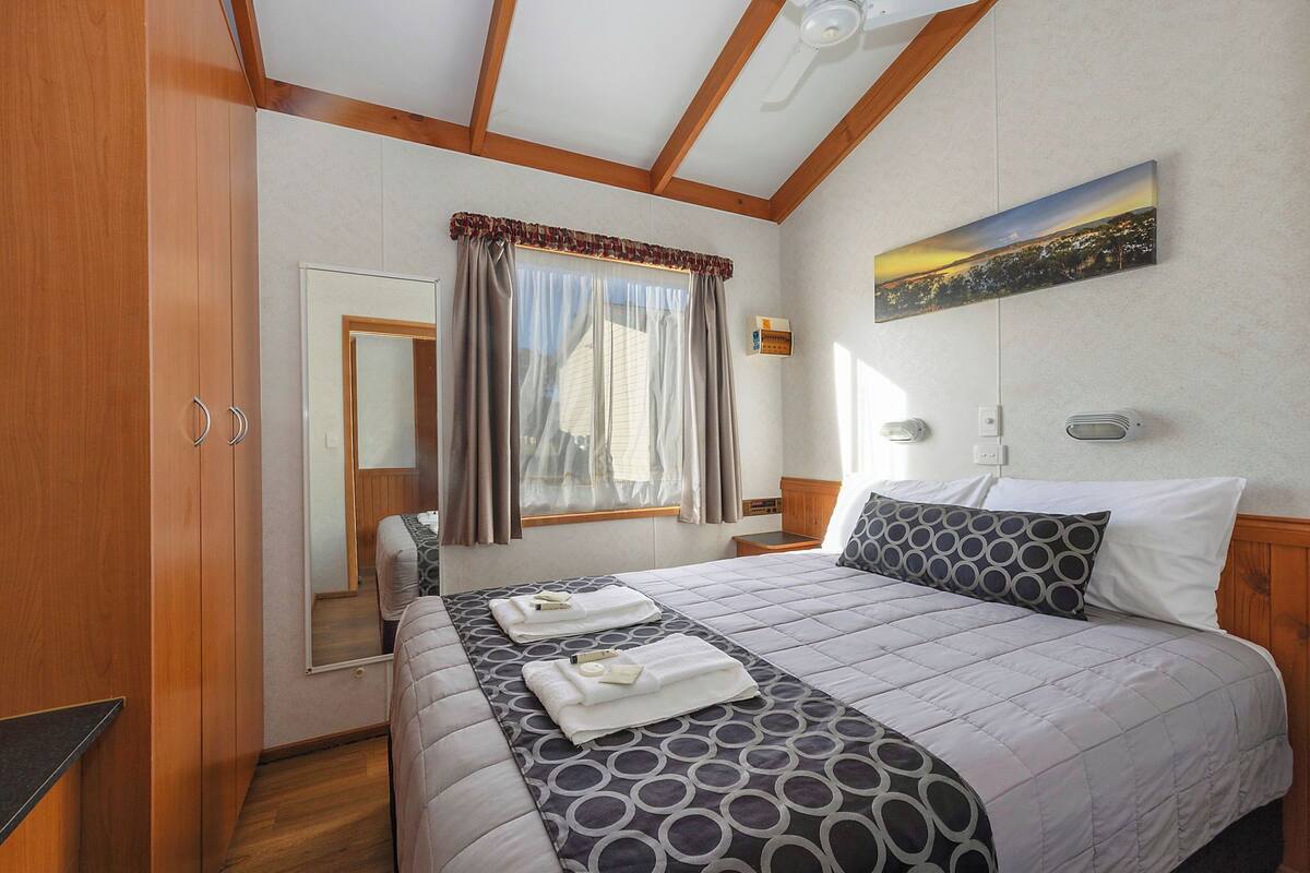 Ein Schlafzimmer mit einem Bett, einem Fenster mit Vorhängen, einem Bild an der Wand und einer Holzbalkendecke.
