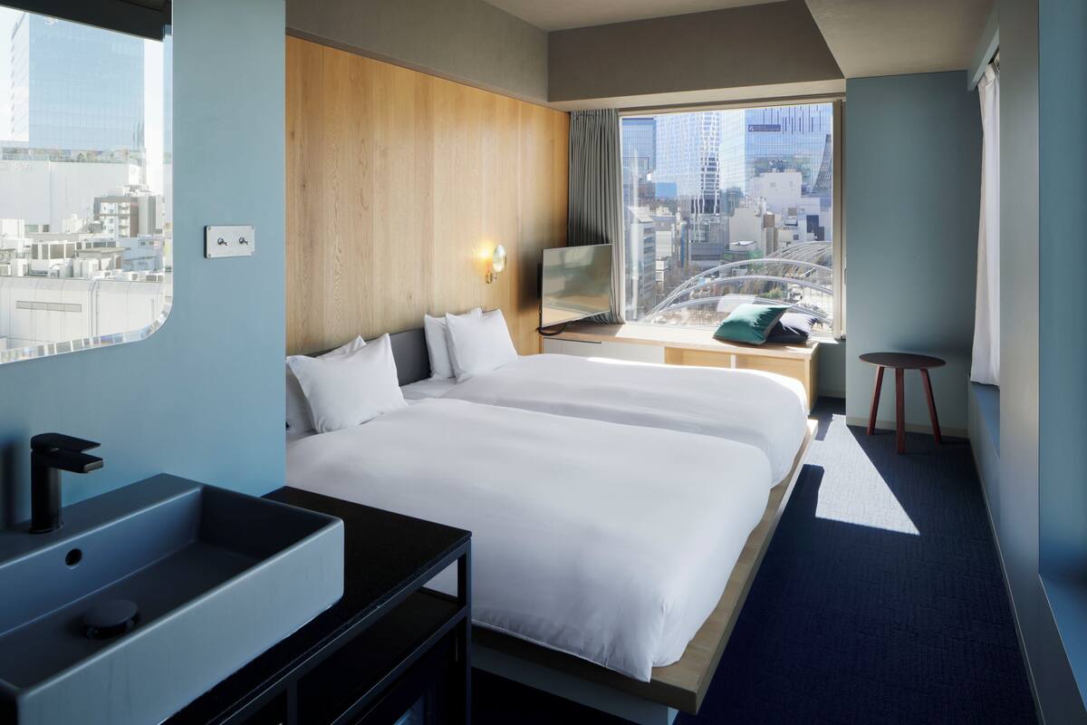 A hotel room with a large bed, a desk with a laptop, a sink, and a view of the city.