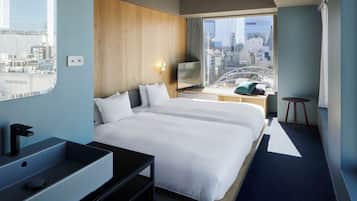 A hotel room with a large bed, a desk with a laptop, a sink, and a view of the city.