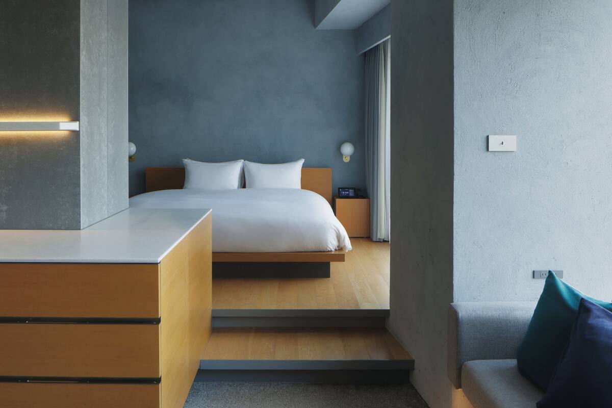 A modern hotel room with a bed, bedside table, and a built-in desk.
