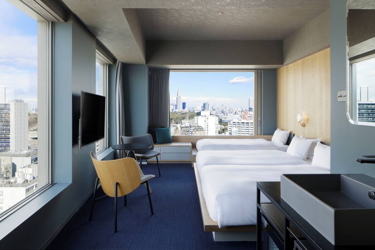 A hotel room with a large bed, a desk, a chair, a TV, and a city view.