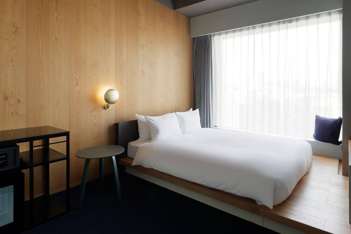 A hotel room with a bed, a desk, a television, and a window with curtains.