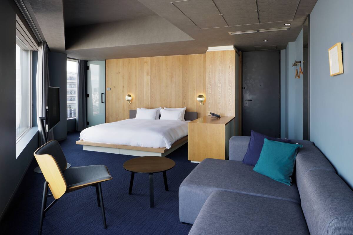 A modern hotel room with a large bed, a sofa, a small table, and a chair.