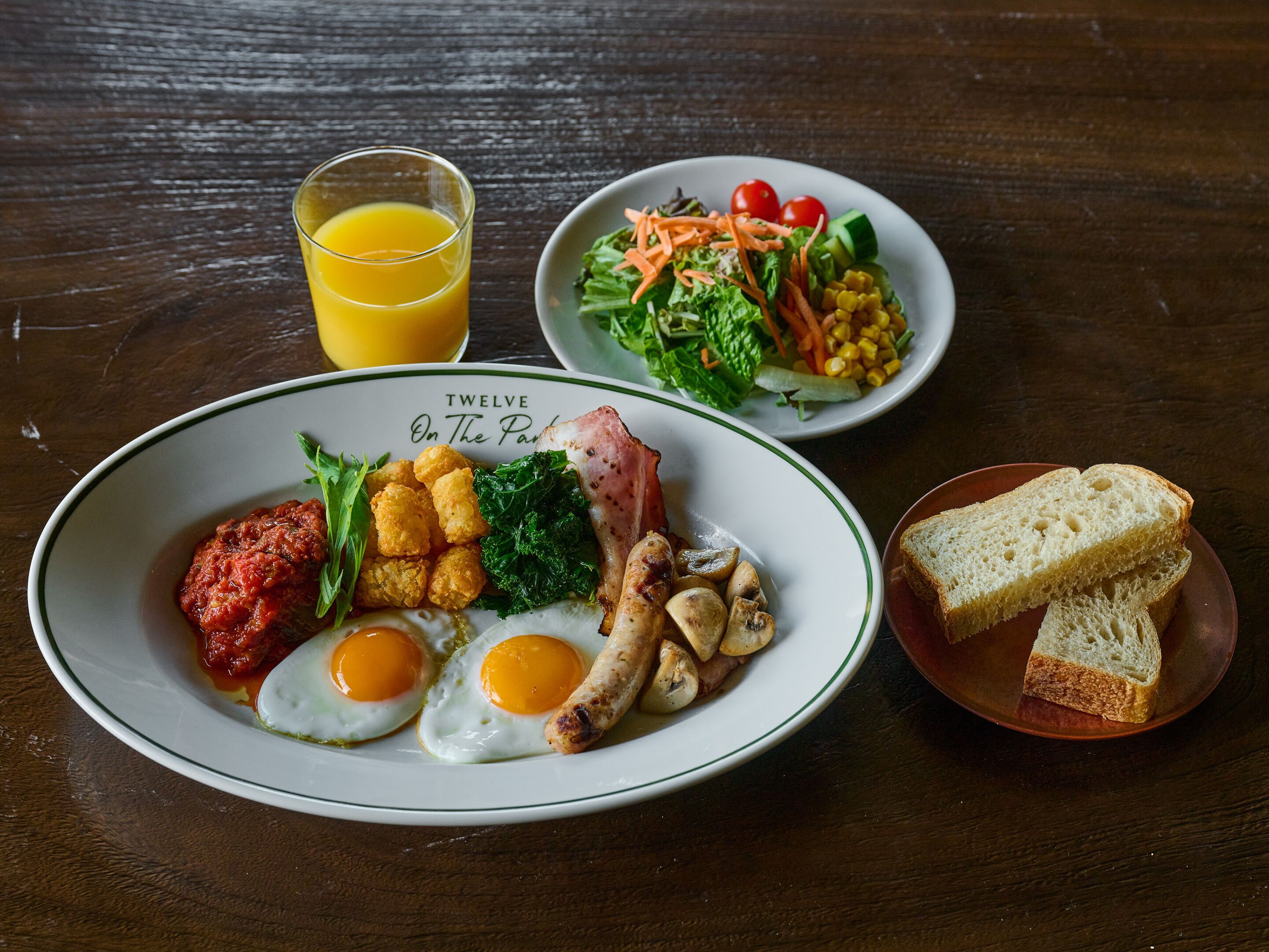 A breakfast plate with eggs, bacon, mushrooms, tater tots, and tomato sauce.