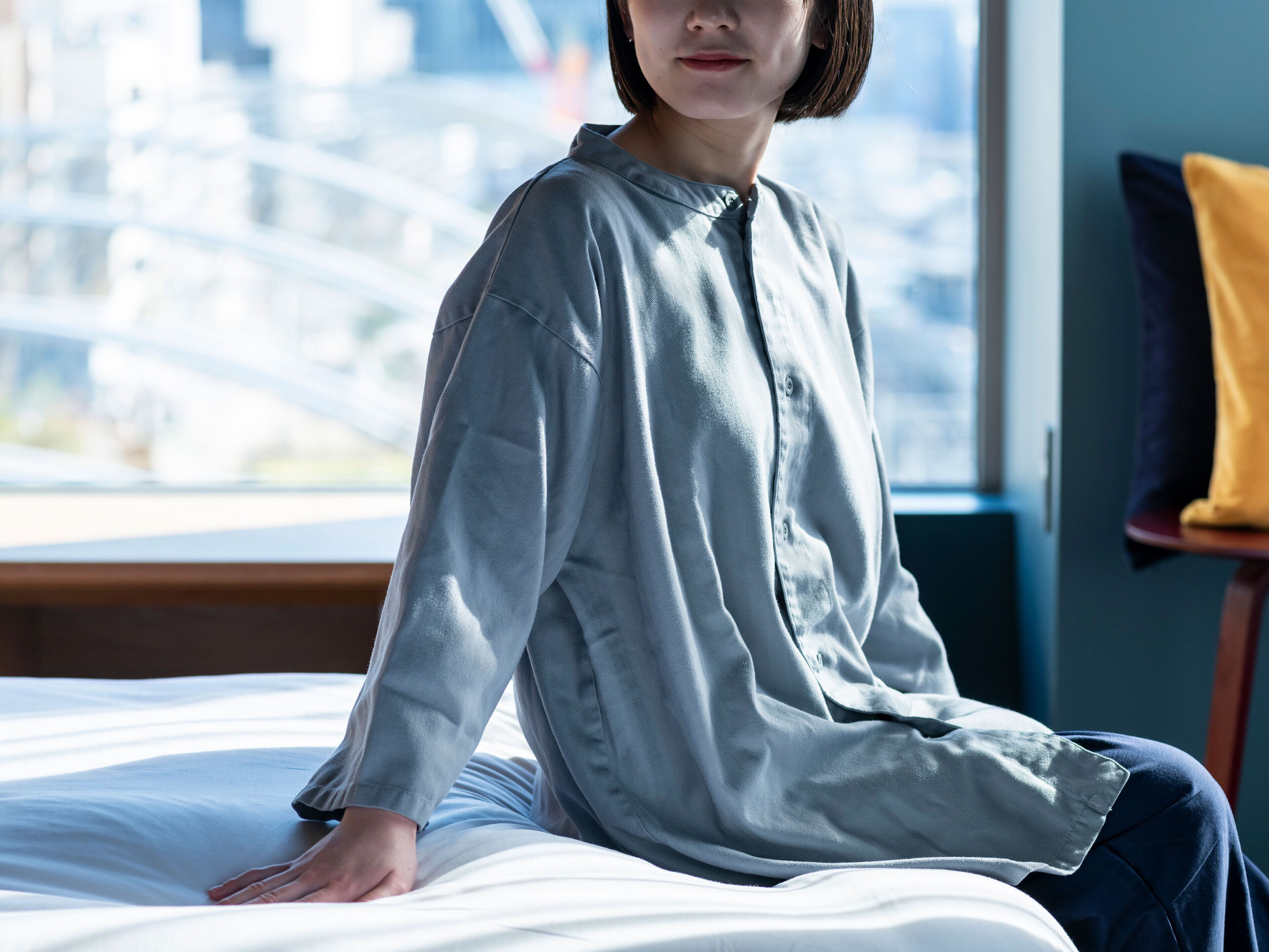 A person sitting on a bed in a room with a view of a cityscape through a window.
