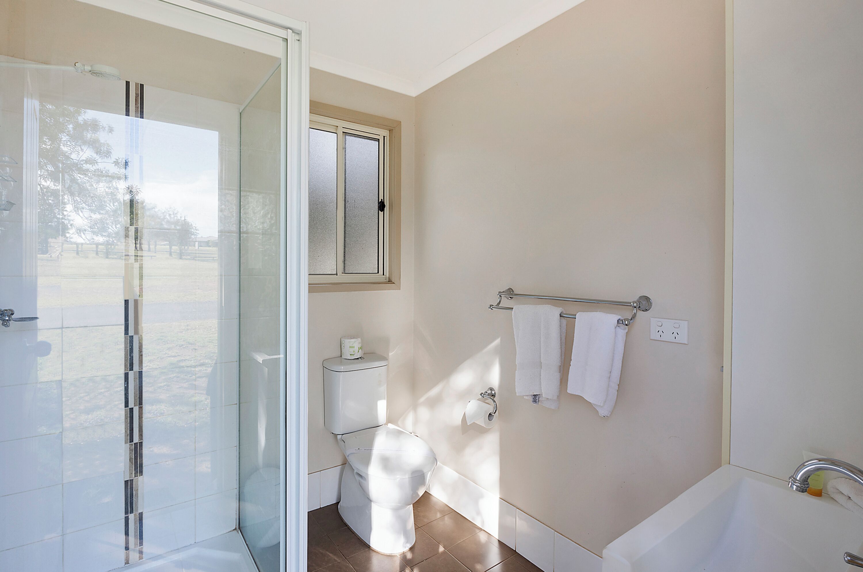 Un baño moderno con cabina de ducha de vidrio, inodoro, bañera y ventana.