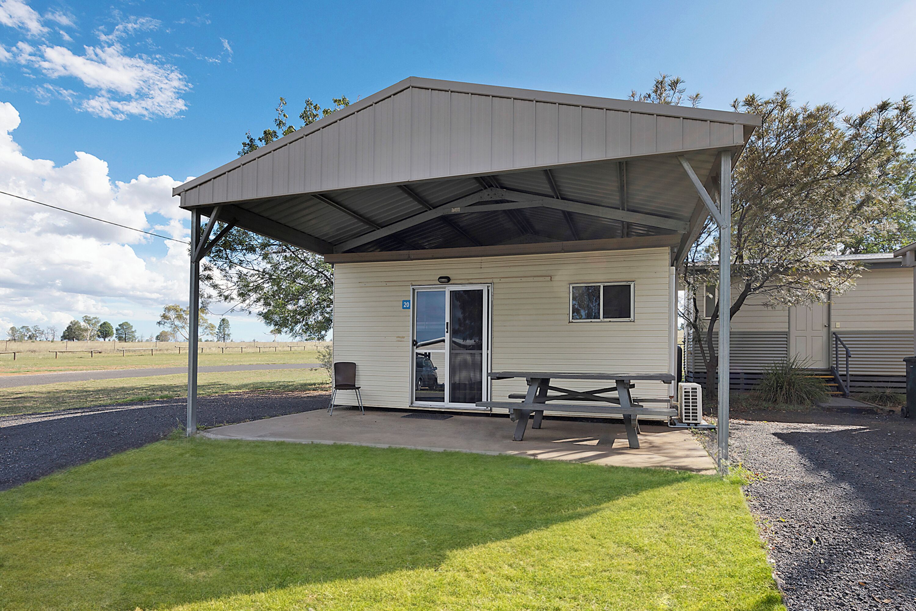 A small, single-story building with a covered patio area, a picnic table, and a chair.