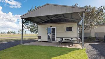A small, single-story building with a covered patio area, a picnic table, and a chair.