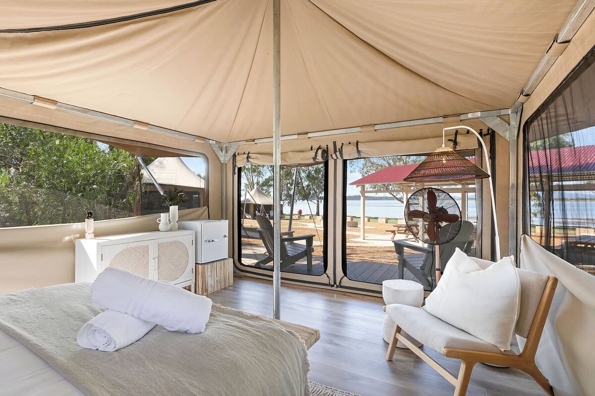 A tented room with a bed, a chair, a table, and a fan.