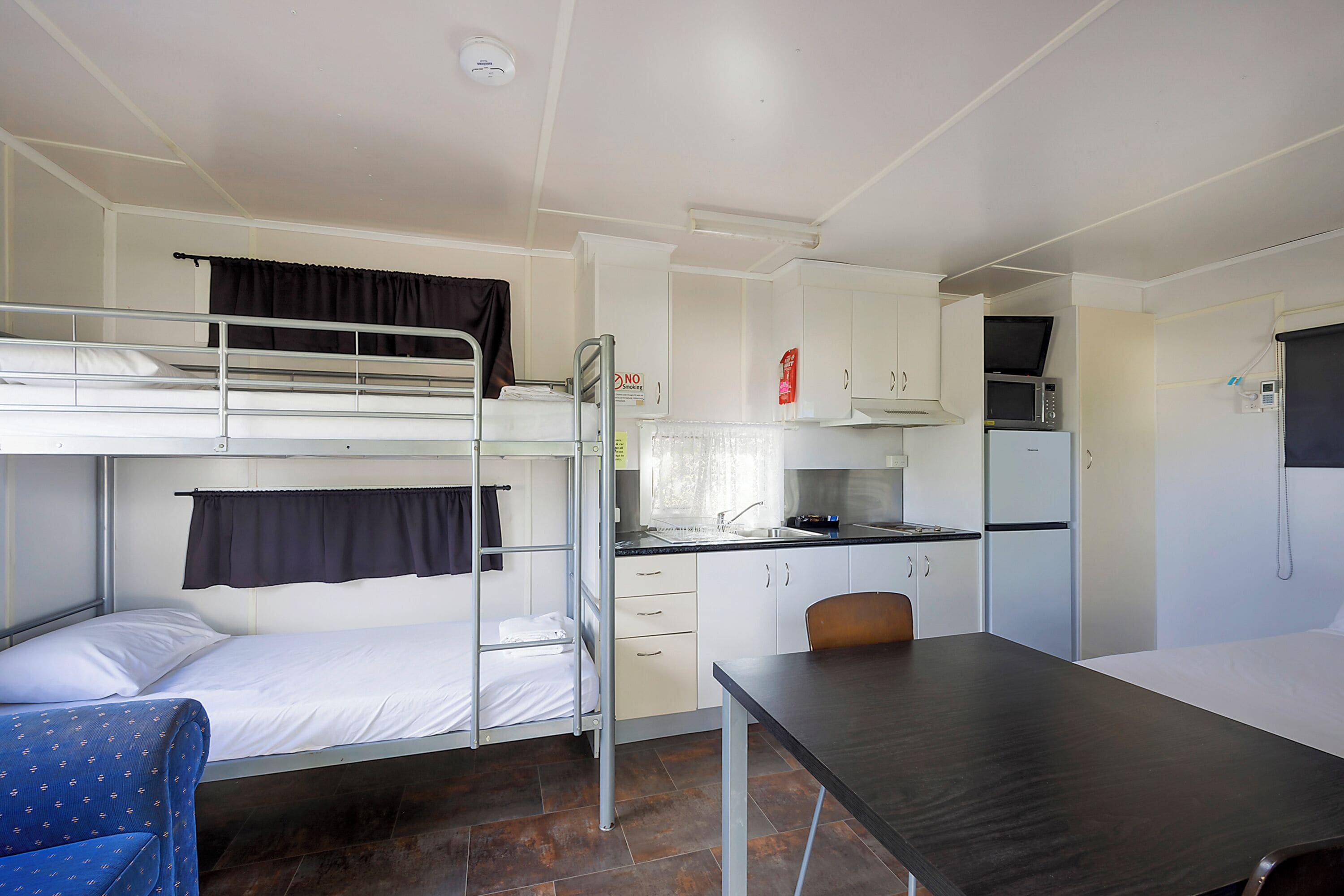 Una habitación pequeña con literas, kitchenette, una mesa de comedor y una silla.