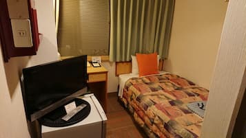 A small hotel room with a bed, a desk with a computer, a TV, and a window with curtains.