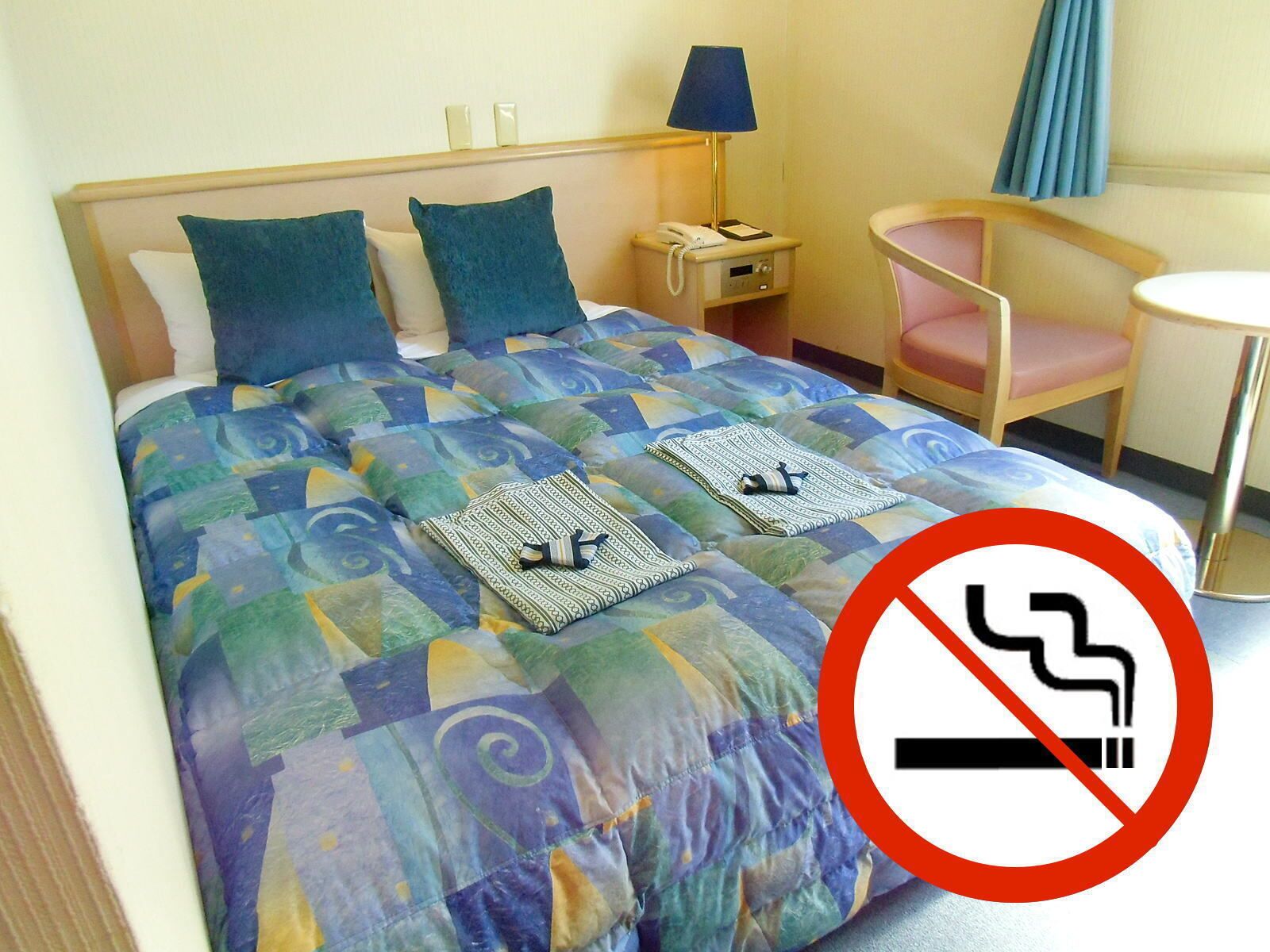 Una habitación de hotel con una cama, una mesita de noche con lámpara, una silla y una pequeña mesa redonda.