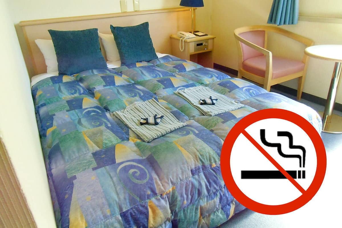A hotel room with a bed, a bedside table with a lamp, a chair, and a small round table.