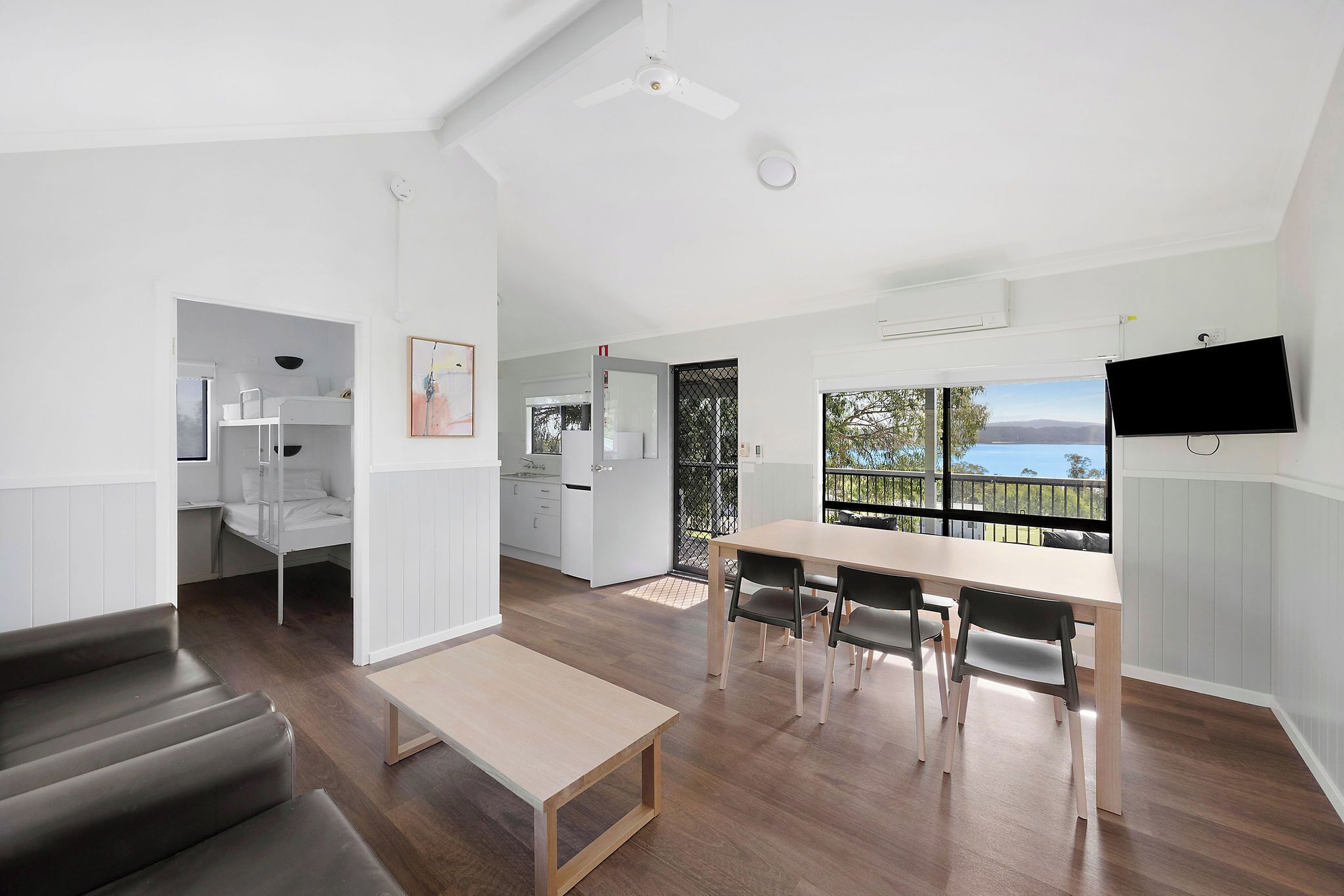 A modern, open-plan living space with a dining area, kitchen, and a balcony with a view.