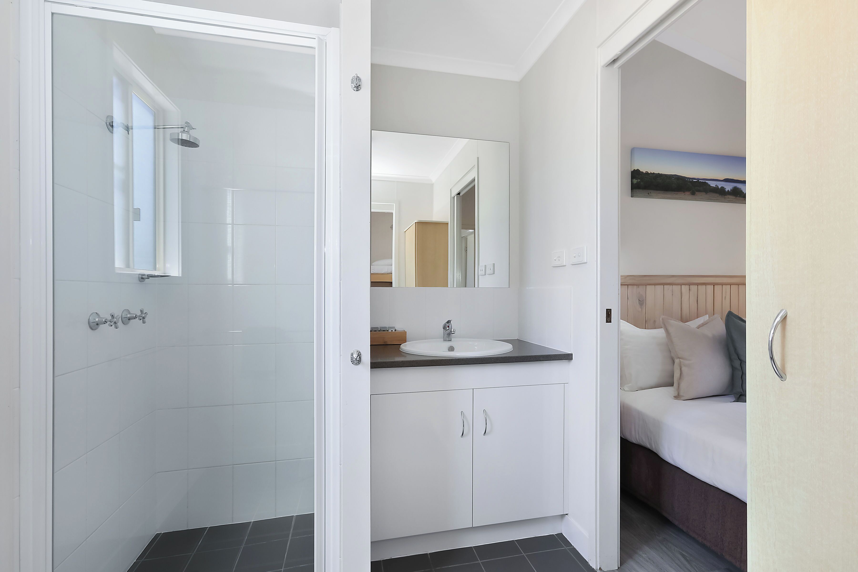 Un baño moderno con mampara de vidrio, un lavamanos blanco y un espejo grande encima.