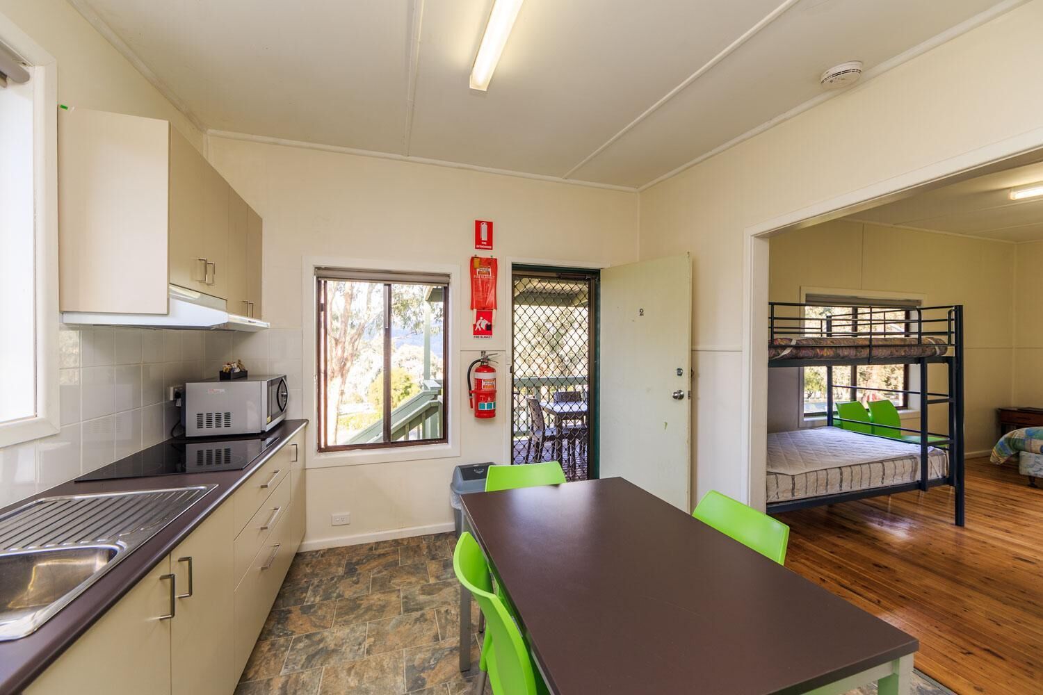 A compact kitchen with a microwave, sink, and cabinets. There's a dining area with a table and chairs, and a bunk bed in the adjacent room.