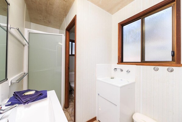 A bathroom with a white sink, a mirror, and a window with a wooden frame.