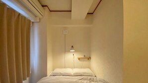 A narrow hotel room with a single bed, a wall-mounted shelf, and a ceiling vent. - Satellite Hotel Komagome (Tokyo)