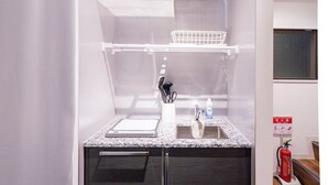 A compact kitchen with a countertop, sink, and cabinets, a ceiling vent, and a fire extinguisher. - Satellite Hotel Komagome (Tokyo)