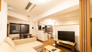 A modern living room with a sofa, a wooden coffee table, a TV, and a kitchen area in the background. - Satellite Hotel Komagome (Tokyo)