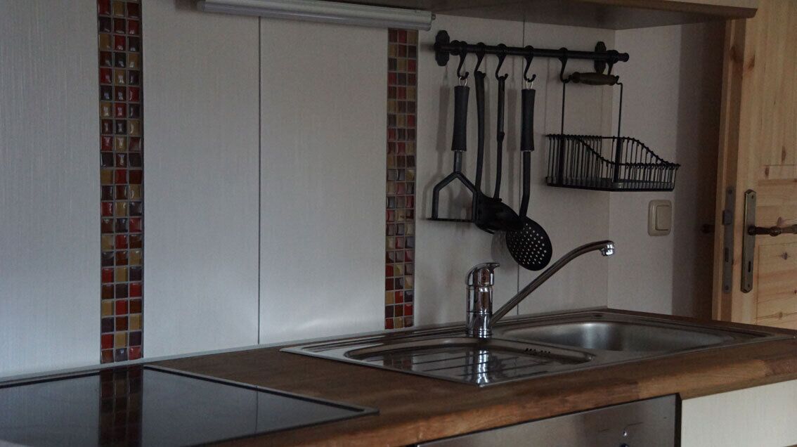 A kitchen with a stainless steel sink, a hanging pot rack, and a backsplash with red and white tiles.