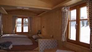 A cozy wooden cabin room with two beds, a bench, and large windows with curtains.