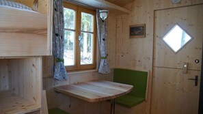 A cabin interior with a wooden table, green bench, window with curtains, and a door with a window.