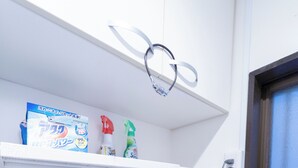 A front-loading washing machine with a control panel, a shelf above it holding cleaning supplies, and a window to the right. - Satellite Hotel Yoyogi Sangubashi (Tokyo)