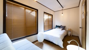 A compact hotel room with two beds, a small bedside table, a white chair, and a bathroom with a shower. - Satellite Hotel Yoyogi Sangubashi (Tokyo)