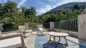 A balcony with wooden furniture, a patterned mat, and a view of a forested hillside. - Gîte "U Caseddu (Ortiporio)