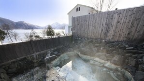 Une zone de sources chaudes entourée d’une clôture en bois, de murs en pierre, et offrant une vue sur les montagnes et un lac.