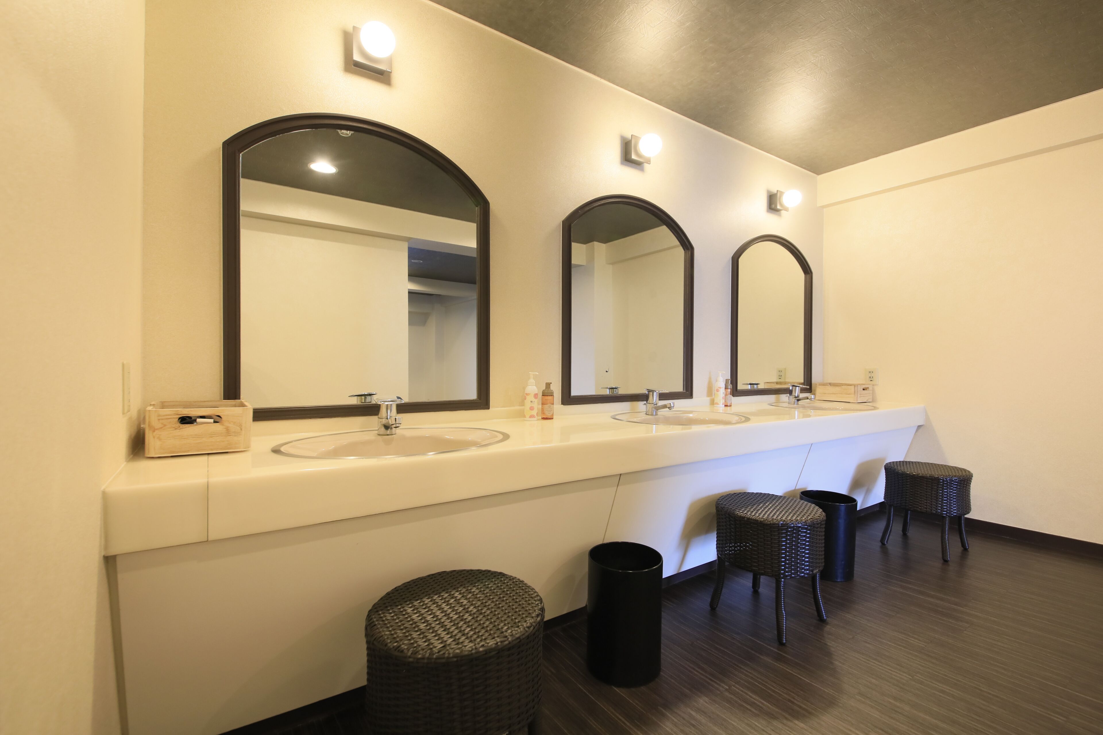Un baño moderno con dos lavamanos, tres espejos y dos taburetes de mimbre.