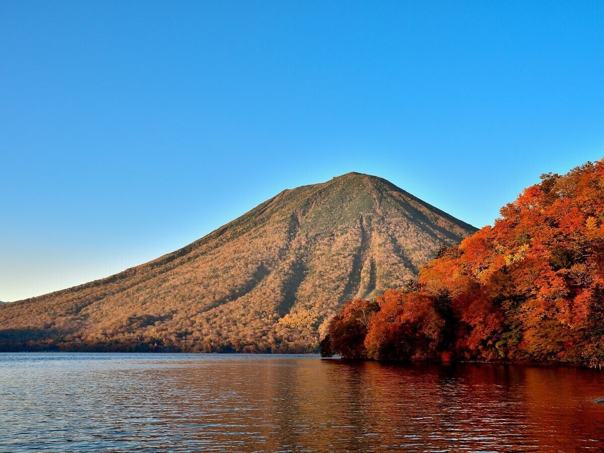 Ein Berg mit Herbstlaub neben einem ruhigen See.