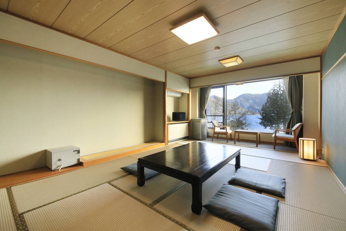 A traditional Japanese room with tatami flooring, a low table, and a view of mountains through a large window.