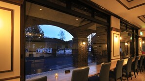 A restaurant with a long table and chairs, a candle on the table, and a view of the street outside. - YUTORELO NIKKO - Hostel (Nikko)
