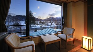 Une pièce avec une grande fenêtre, deux chaises, une petite table et un lampadaire.