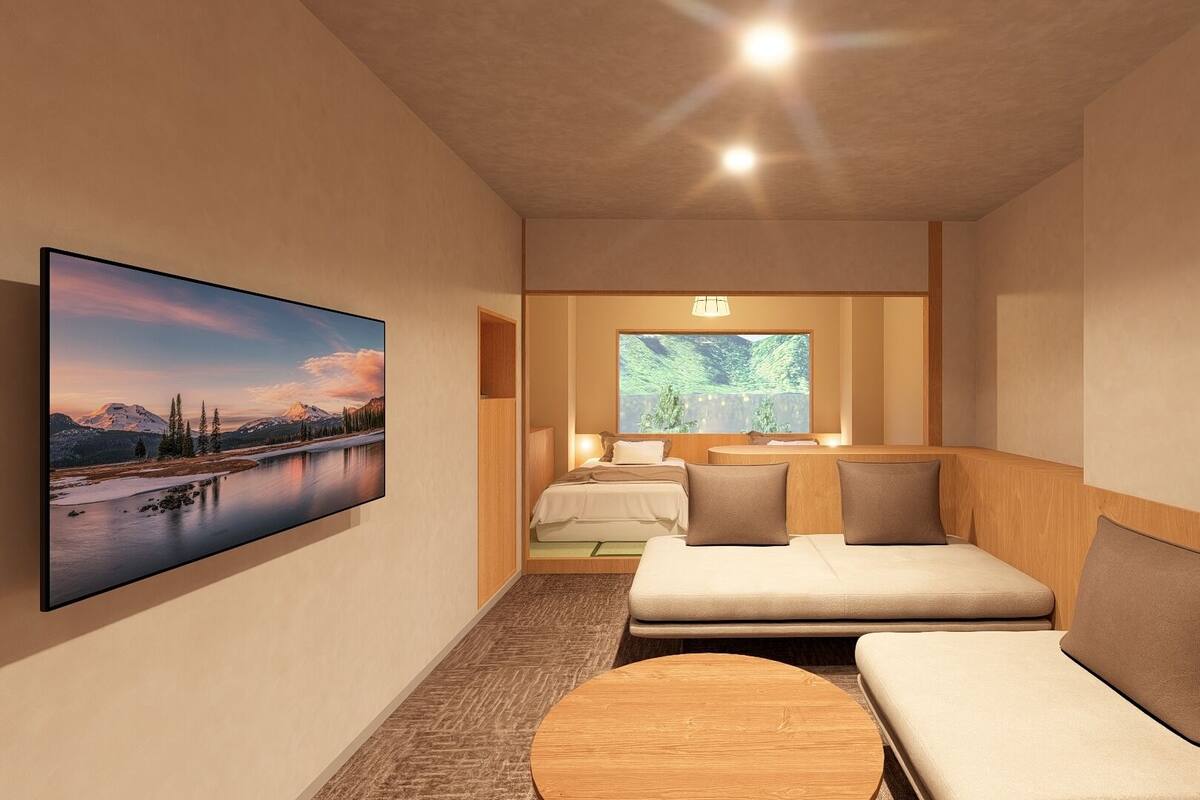 A modern hotel room with a large bed, a sofa, a small table, and a large window with a view of trees.