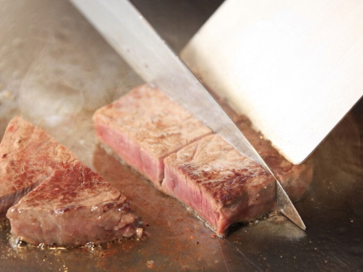 A steak being sliced on a metal surface.