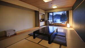 Une pièce de style japonais traditionnel, avec un sol recouvert de tatamis, une table basse, un canapé et une vue sur les montagnes par une grande fenêtre.