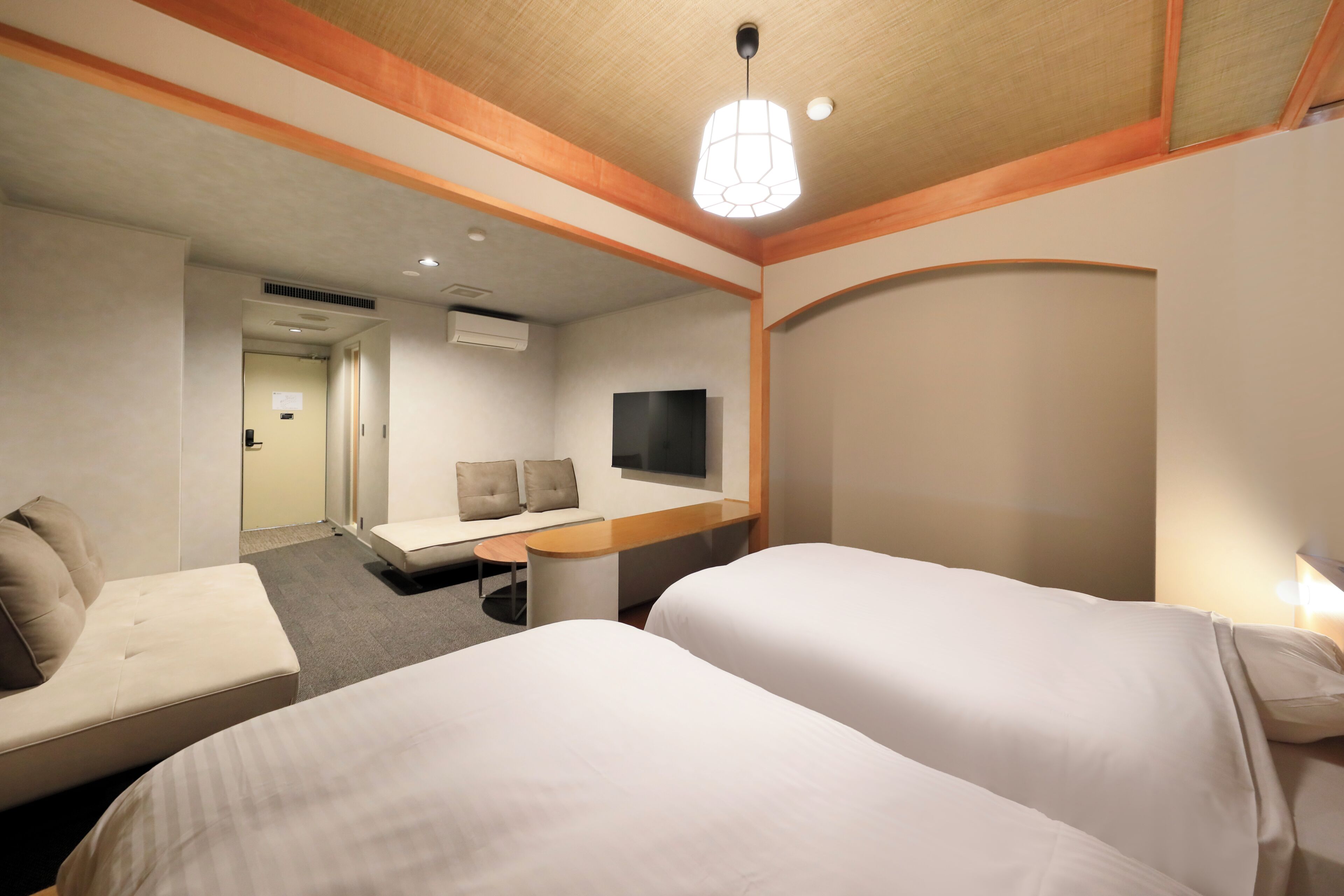 A hotel room with two beds, a desk, a TV, and a seating area.