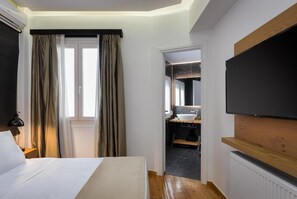 Une chambre d’hôtel avec un lit, une télévision, une salle de bain avec un lavabo et un miroir, et un plancher en bois.