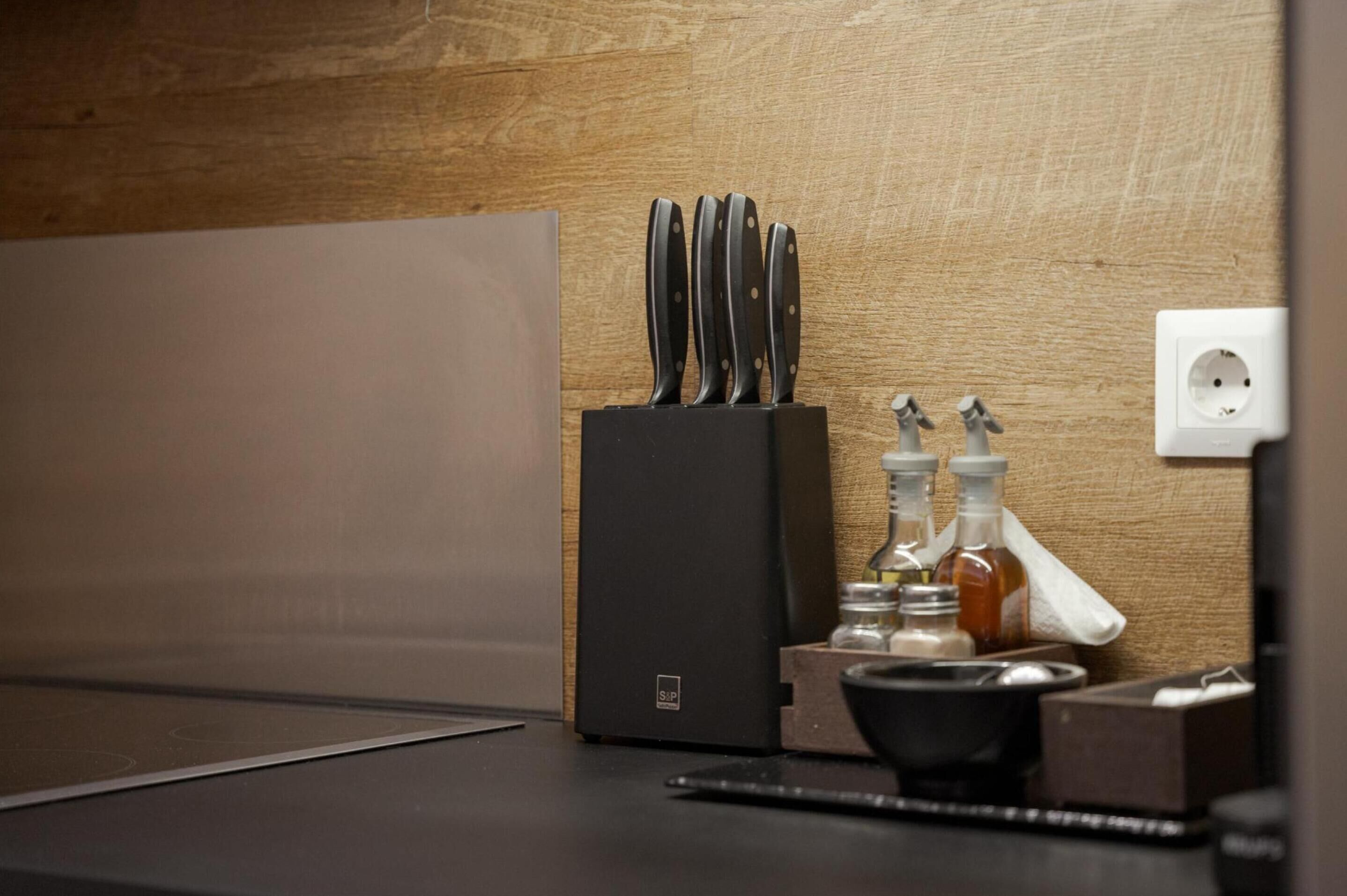 A kitchen counter with a black knife block, two bottles of condiments, and a power outlet.