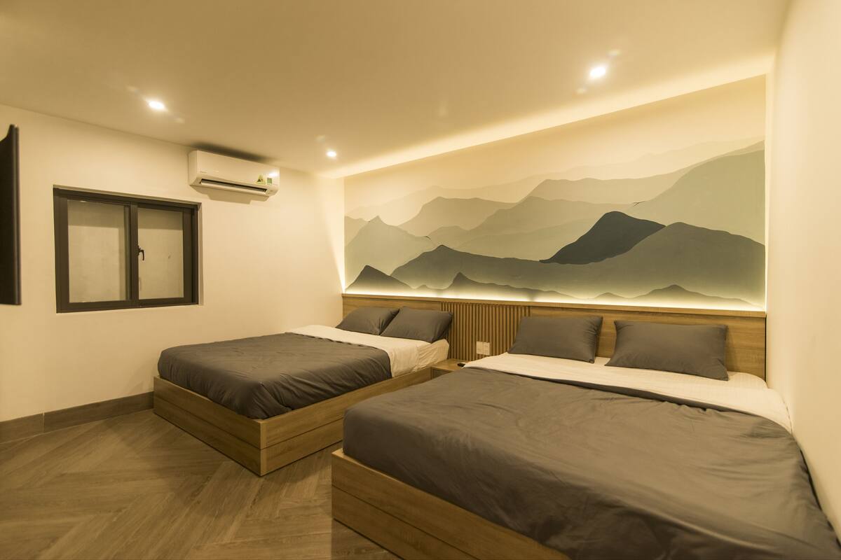 Habitación de hotel con dos camas, un gran mural en la pared de montañas y un equipo de aire acondicionado.