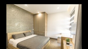 Un dormitorio moderno con una cama de madera, un colchón gris, cabecera gris, un armario, una mesita de noche con una planta y un televisor en la pared.