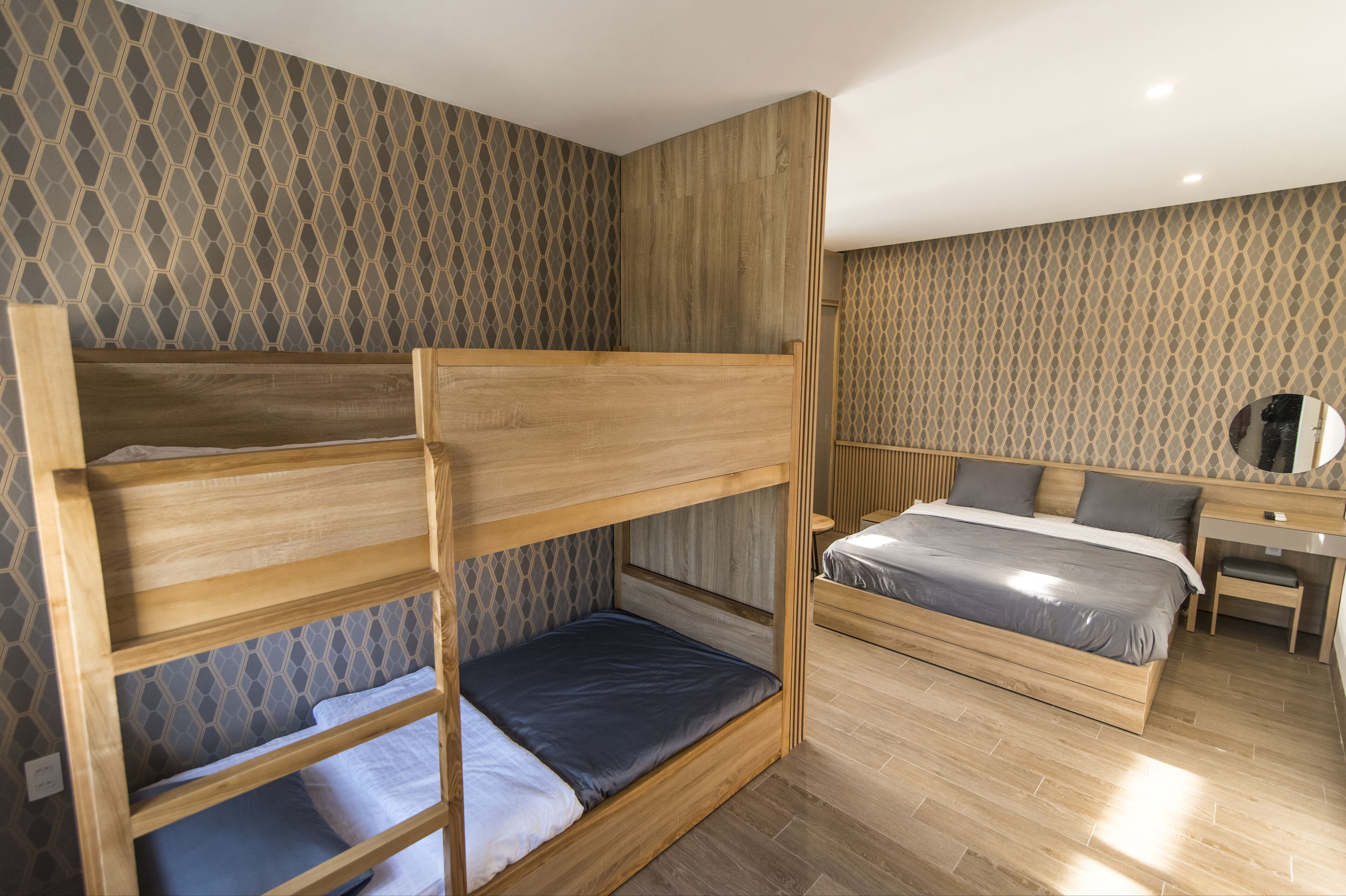 A bunk bed with a desk and a bed in a room with patterned wallpaper.