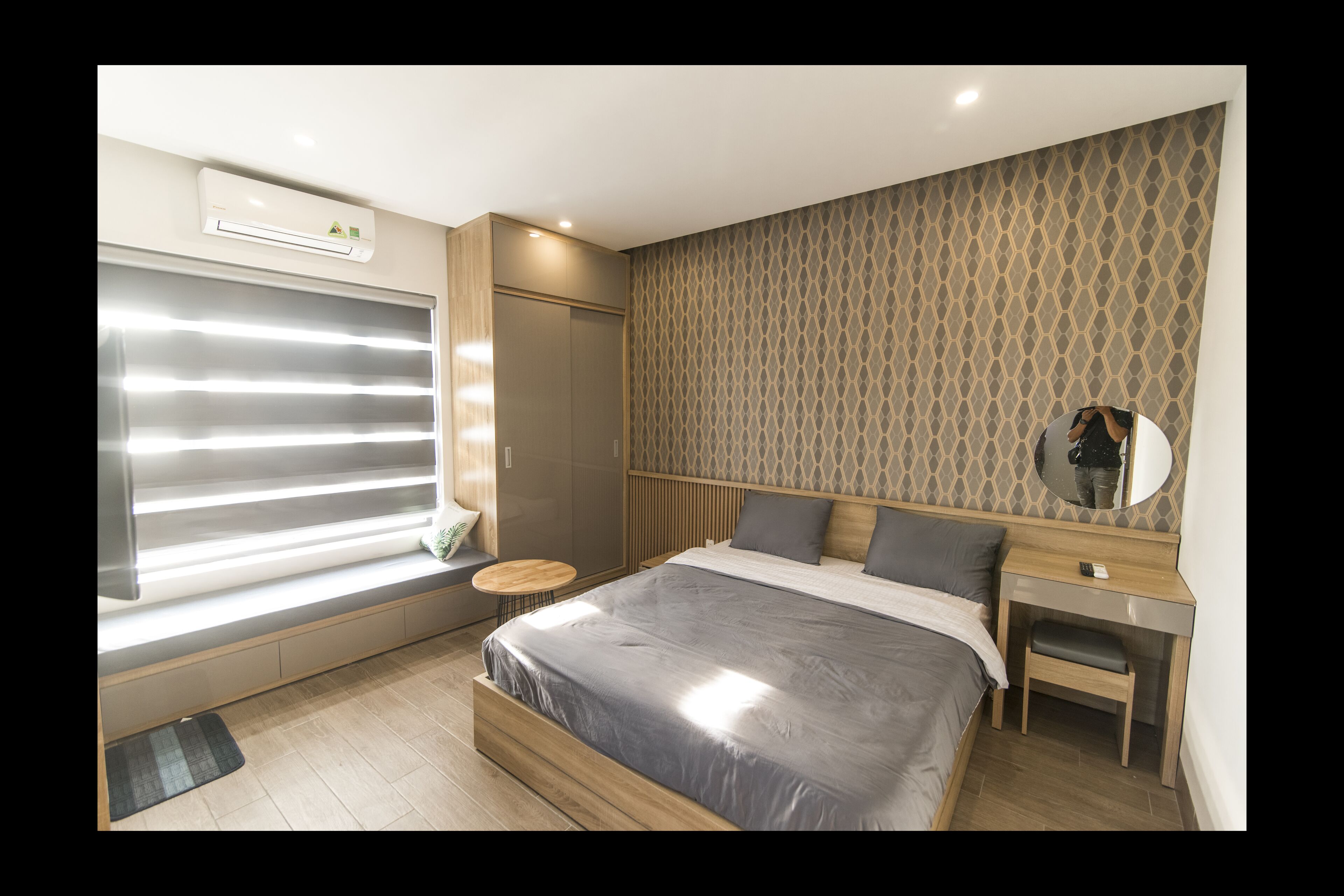 A modern bedroom with a large bed, a desk, a small round table, and a window with blinds.